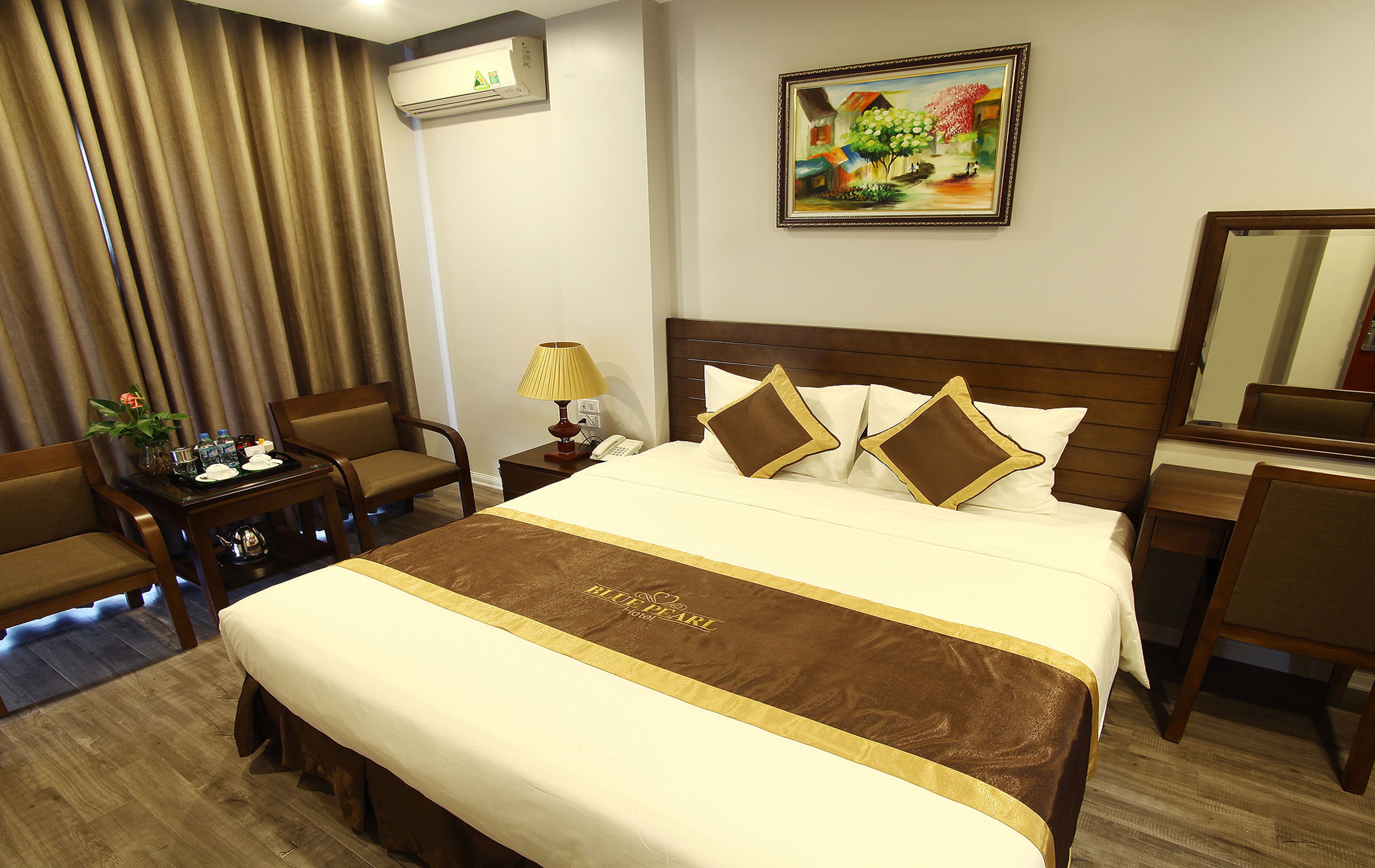 A hotel room with a large bed, a desk, a chair, a lamp, and a painting on the wall.