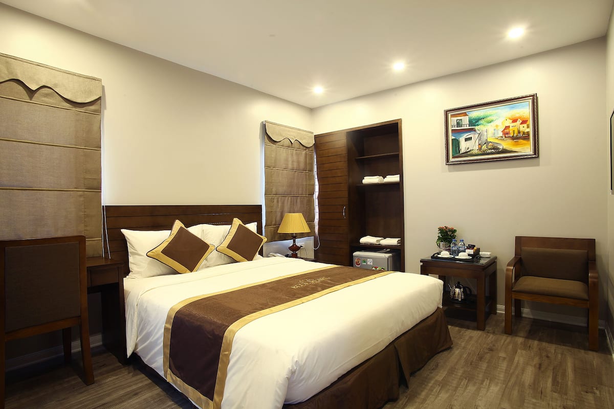 Una habitación de hotel con una cama grande, un escritorio, una silla, un armario y un cuadro en la pared.