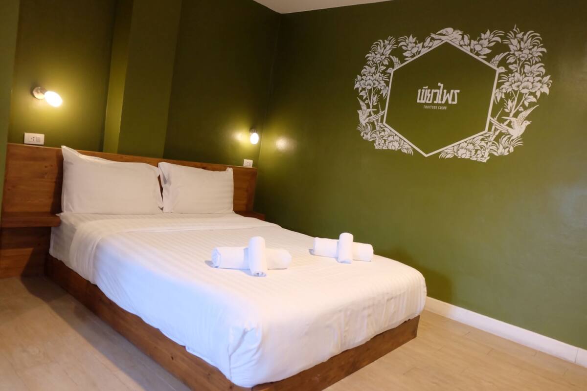 Cama bem arrumada com lençóis brancos e toalhas enroladas, cabeceira de madeira e parede com um desenho floral e o nome "Swan" no canto.