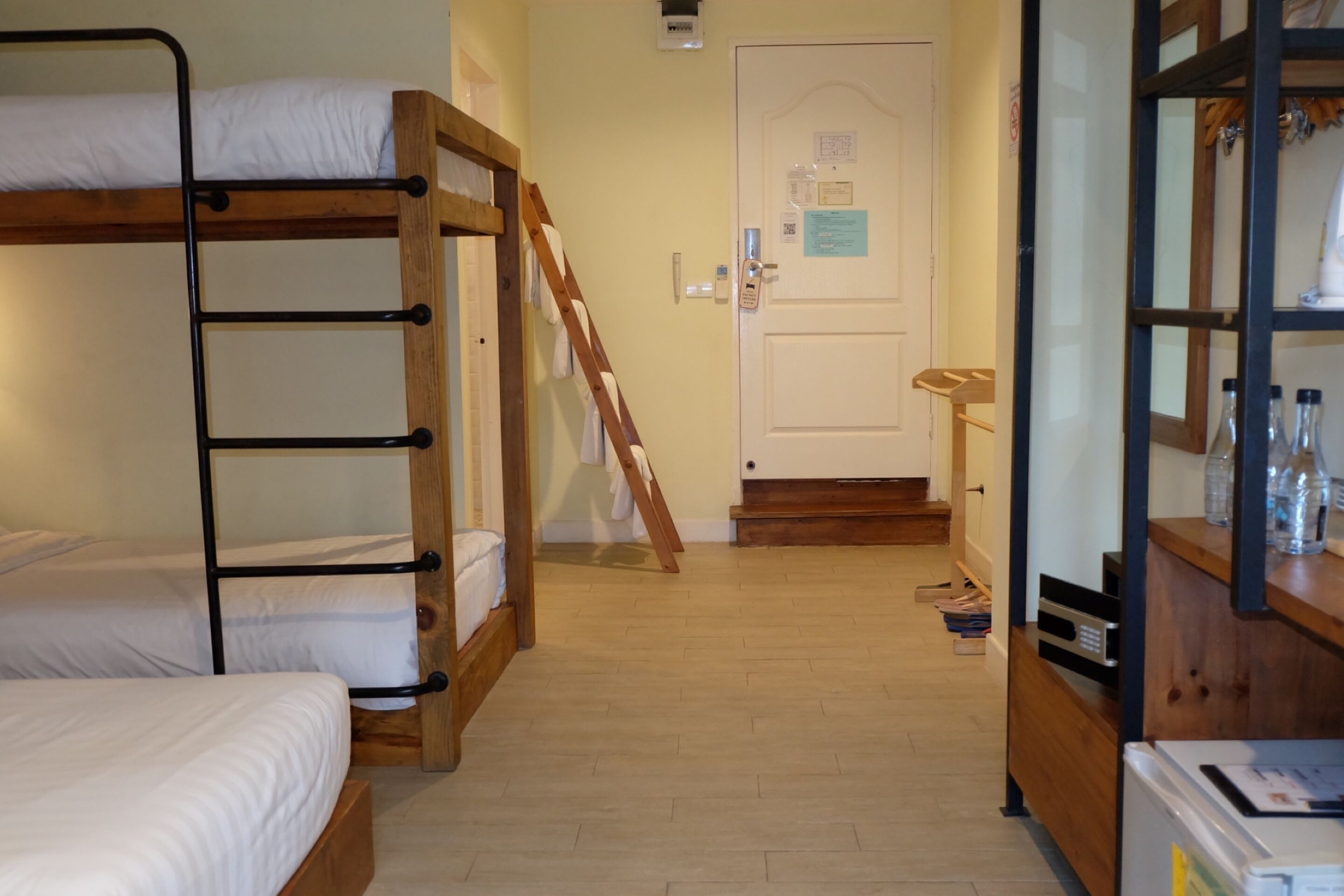 Una habitación con literas, una escalera de madera, una puerta con un aviso y un estante con botellas.