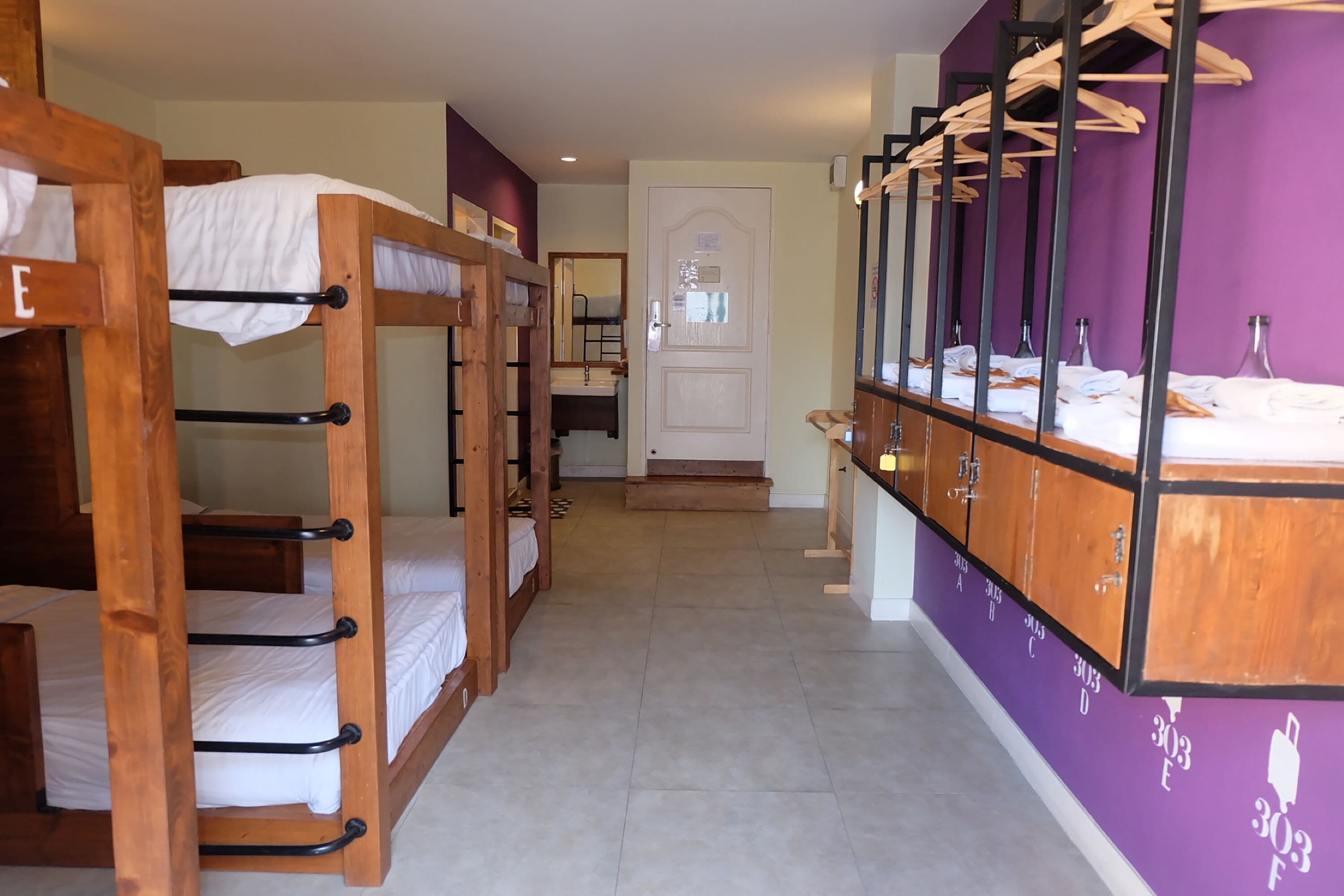A hotel room with bunk beds, a bathroom with a mirror, and a purple wall.