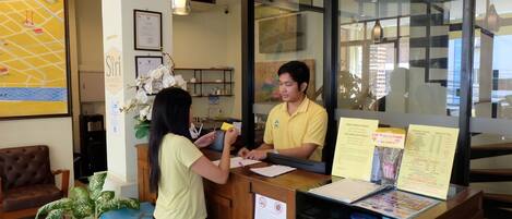 A reception desk with a woman and a man, a map on the wall, and a plant.