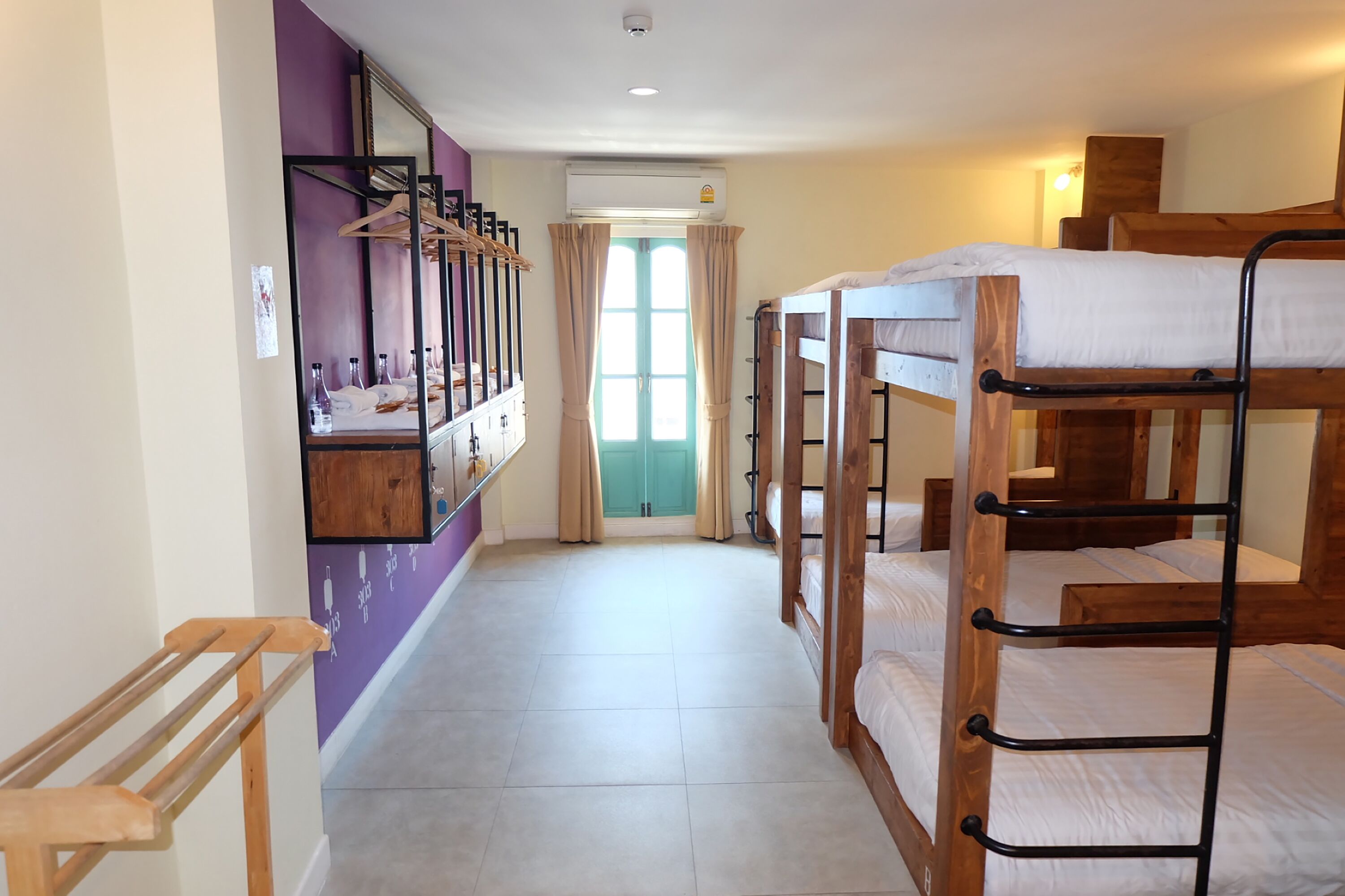 A room with bunk beds, a mirror, a drying rack, and a window with curtains.