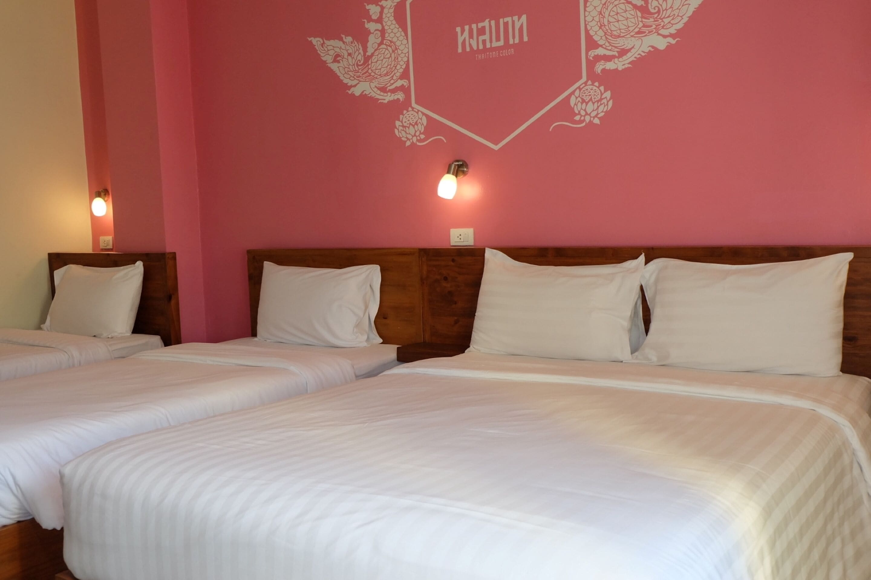 A hotel room with two single beds, wooden headboards, and a pink wall with a decorative emblem.