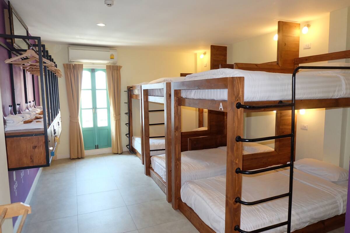 Quarto com beliches de madeira, escada com roupas penduradas e porta com cortinas.