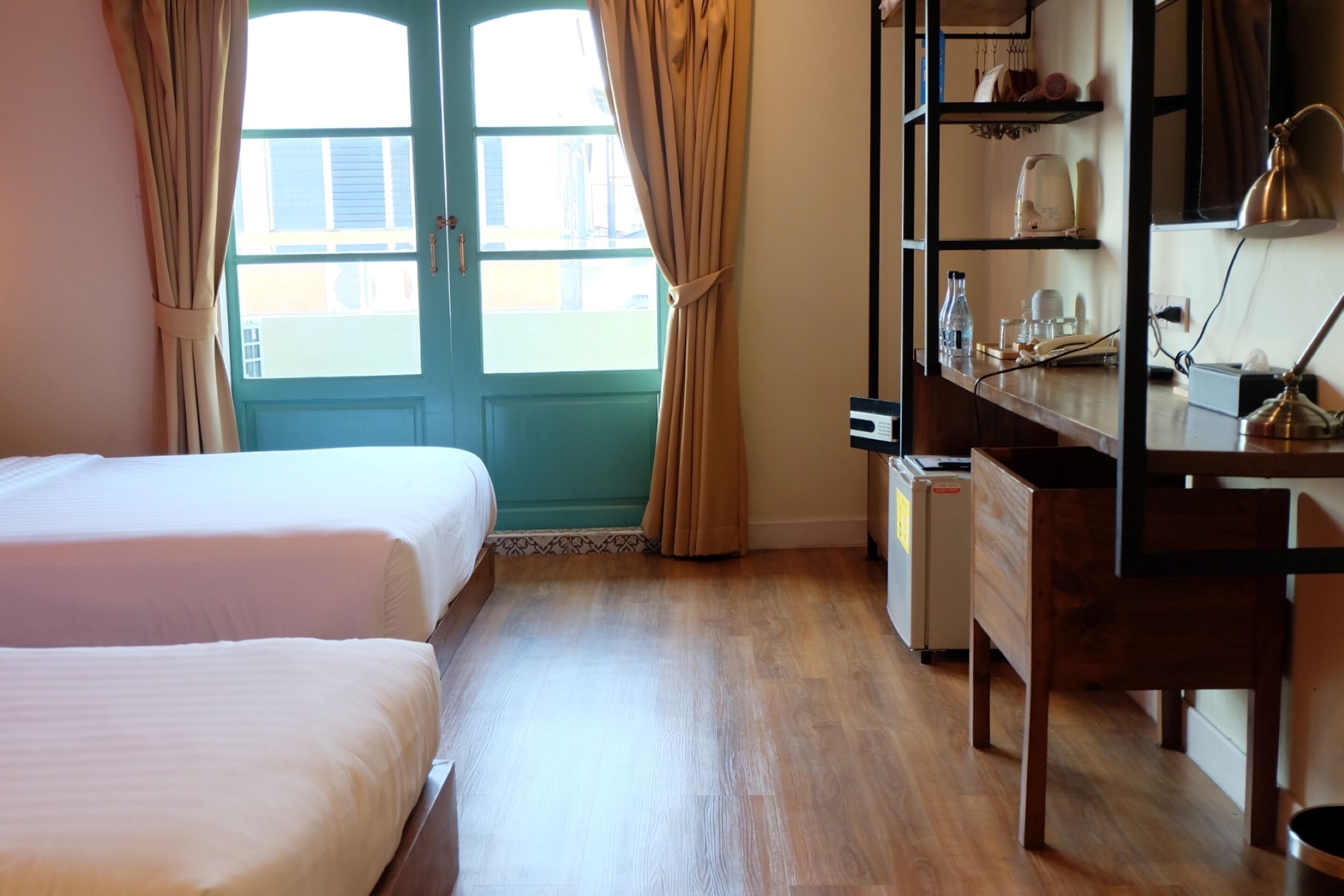 A room with two beds, a desk, a lamp, and a window with curtains.