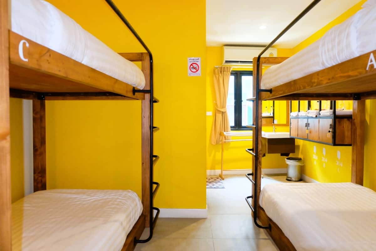 Quarto com beliches identificados com as letras 'C' e 'A', pia pequena e janela com cortinas.