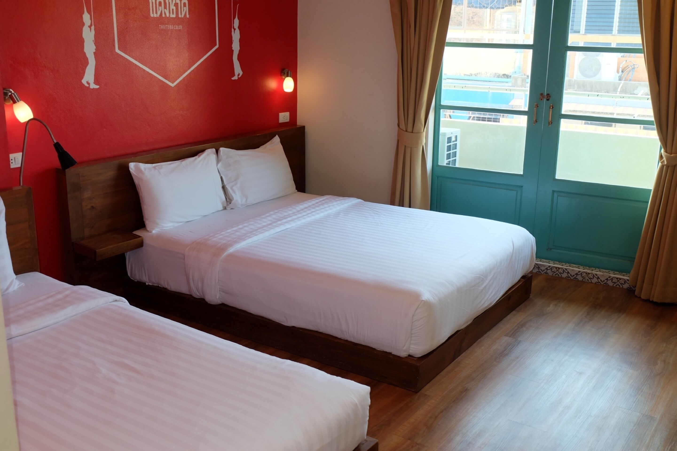 A hotel room with two beds, a red wall with a geometric design, a wooden headboard, and a view of a pool through a door.
