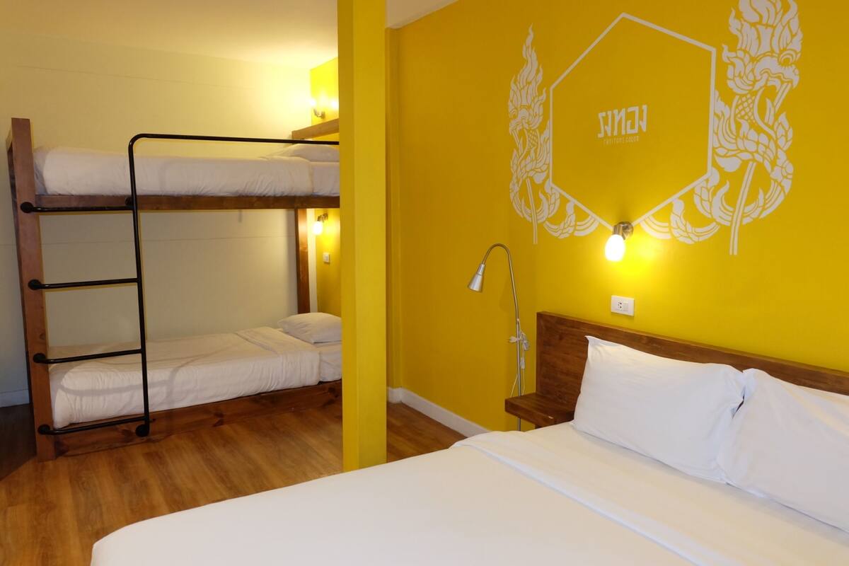Quarto com beliche, uma escada de madeira, mesa de cabeceira com abajur e parede com design geométrico.