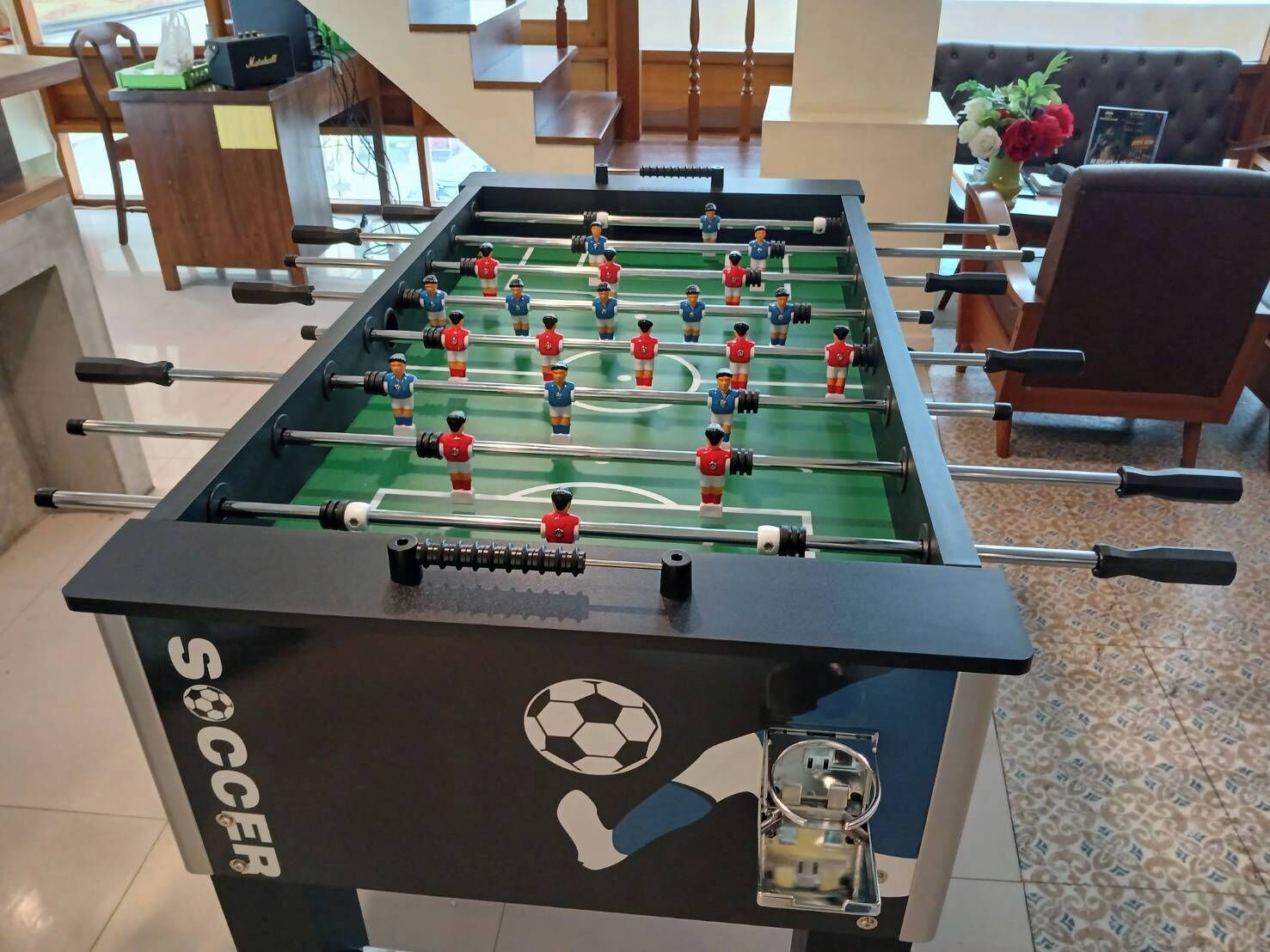 A foosball table with a soccer theme, located in a room with a sofa and a coffee table.