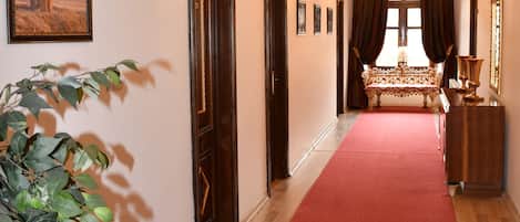 A hallway with a red carpet, wooden flooring, a chandelier, a bench, and a plant.
