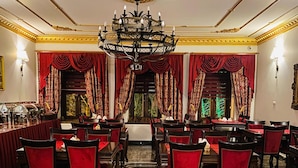 Un comedor formal con piso de mármol, sillas tapizadas en rojo y un candelabro.