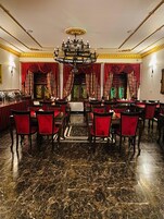 A formal dining room with a marble floor, red upholstered chairs, and a chandelier.
