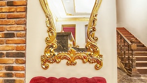 Una habitación lujosa con un espejo grande y ornamentado de oro, un banco rojo acolchado y una escalera.