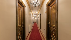 Un pasillo con alfombra roja, puertas de madera con detalles dorados y un candelabro.