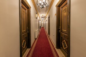 A hallway with a red carpet, wooden doors with gold accents, and a chandelier.