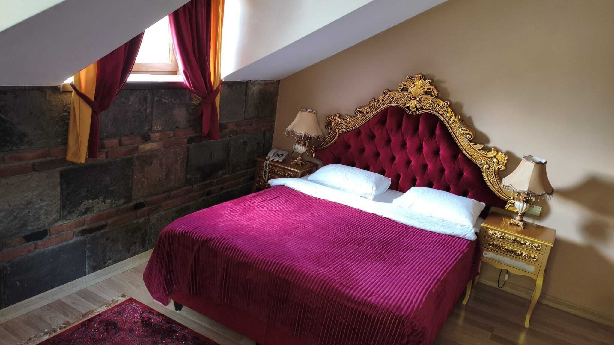 A bedroom with a stone wall, a red velvet bed, and a classic gold headboard.