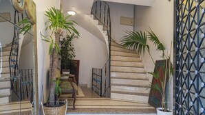 Un escalier avec une rampe, un pot de fleurs et un mur orné d’un motif géométrique.