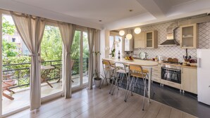 Une cuisine moderne dotée d’un grand îlot central, d’un coin repas avec des chaises et d’une vue sur un balcon aménagé avec du mobilier d’extérieur.