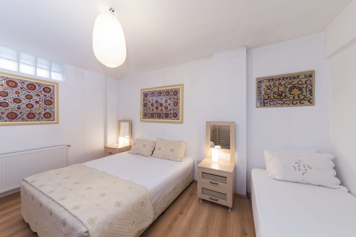 A bedroom with a large bed, a smaller bed, a nightstand with a lamp, and decorative wall art.