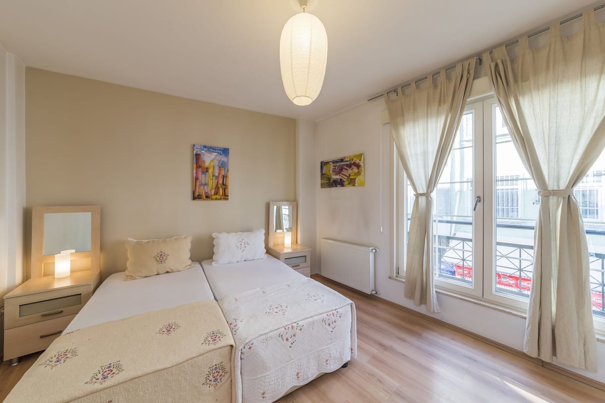 A hotel room with a large bed, bedside tables, a nightstand, a radiator, and a window with curtains.