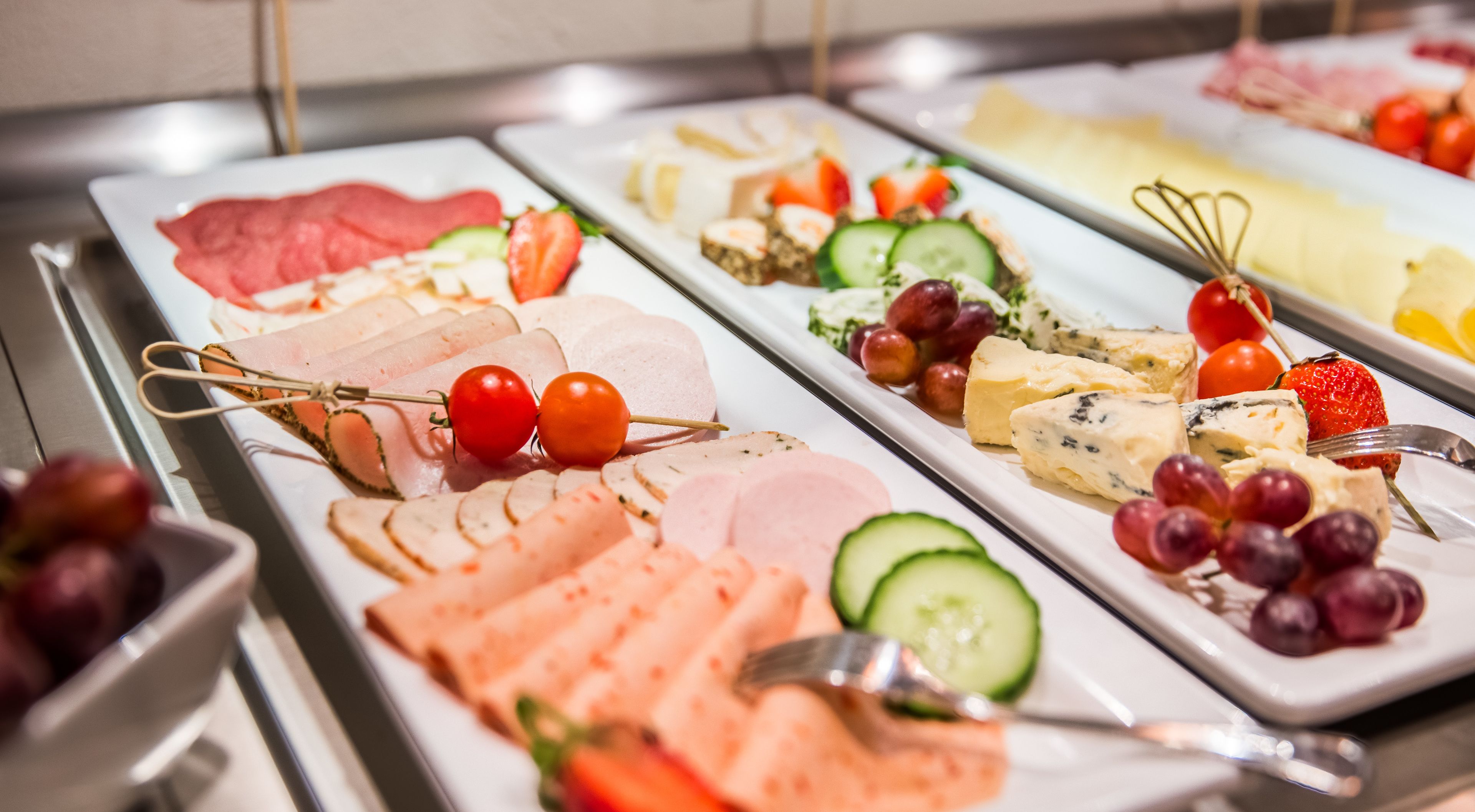 En buffet med et stort udvalg af mad, herunder kød, oste, frugt og grøntsager.