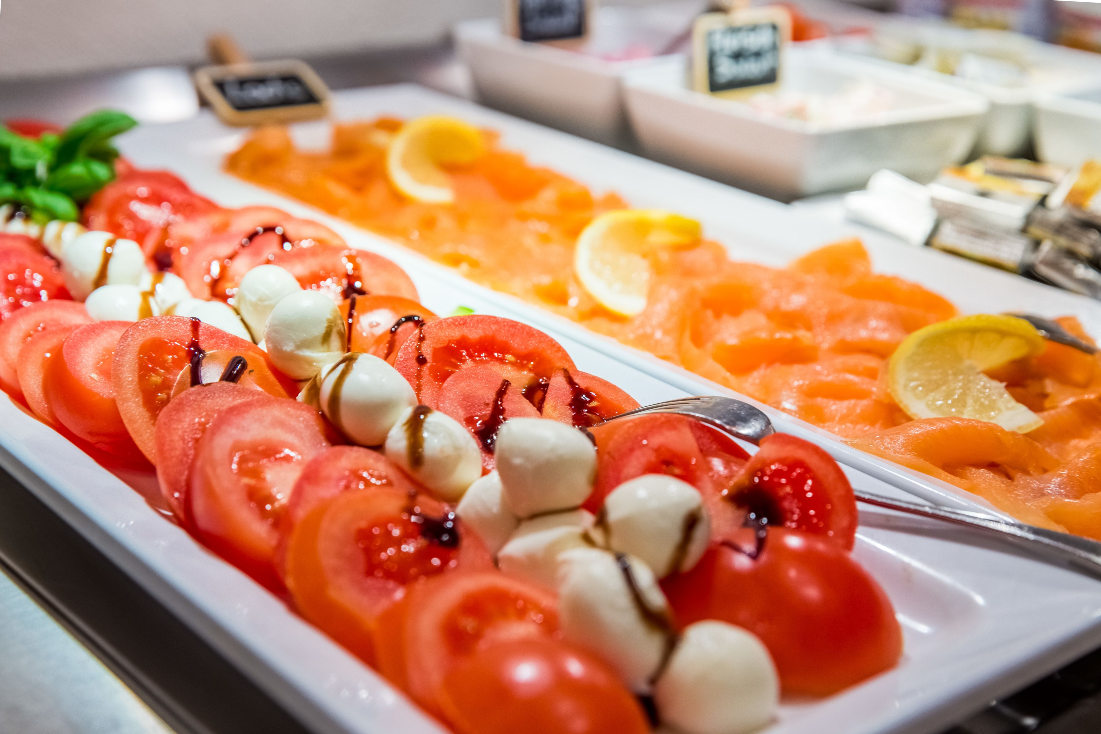Un bufé con diversas opciones de comida, entre ellas, tomates en rodajas, bolas de mozzarella y salmón.