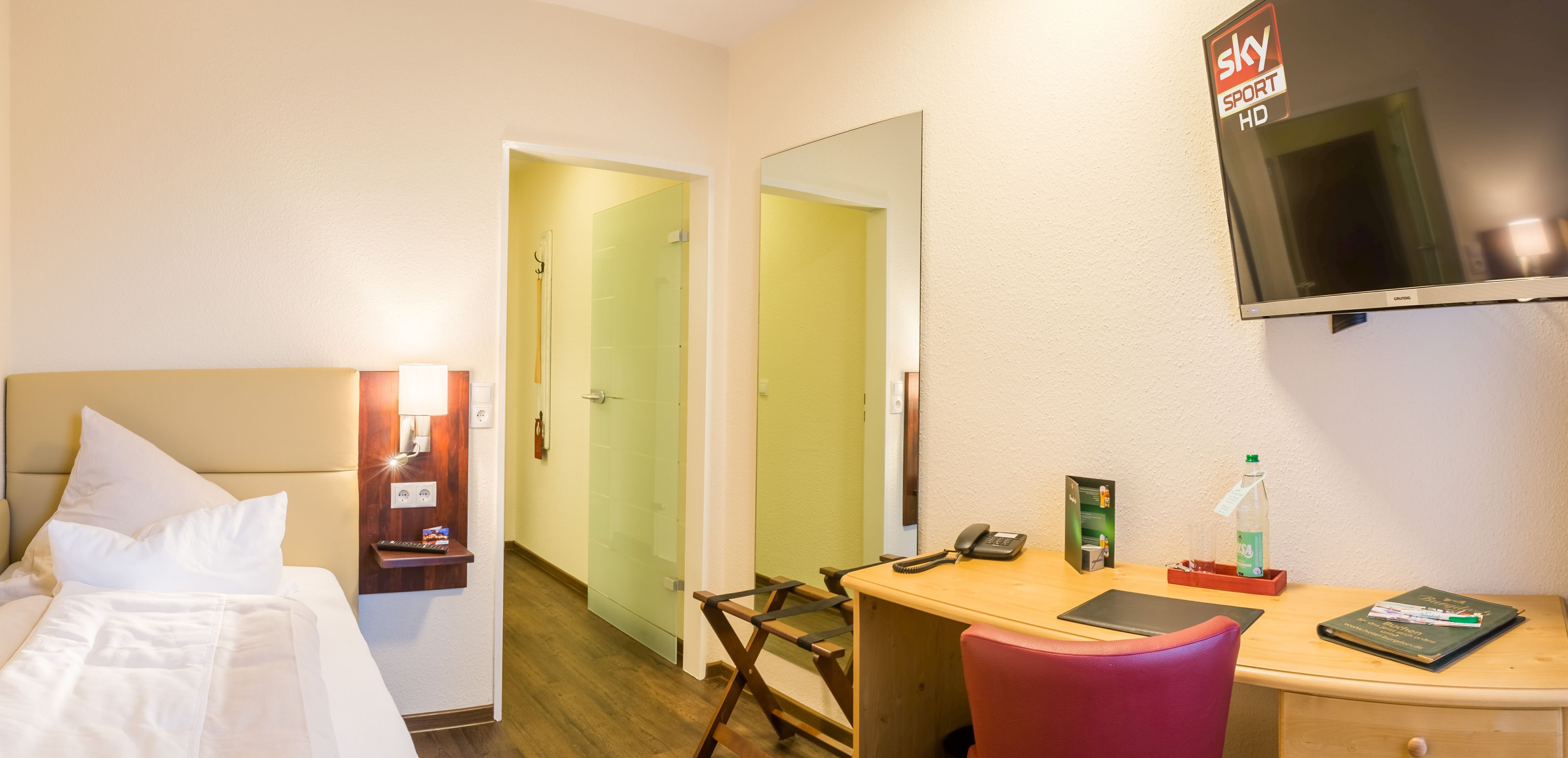Ett hotellrum med en säng, ett skrivbord, en stol, en tv och en spegel.