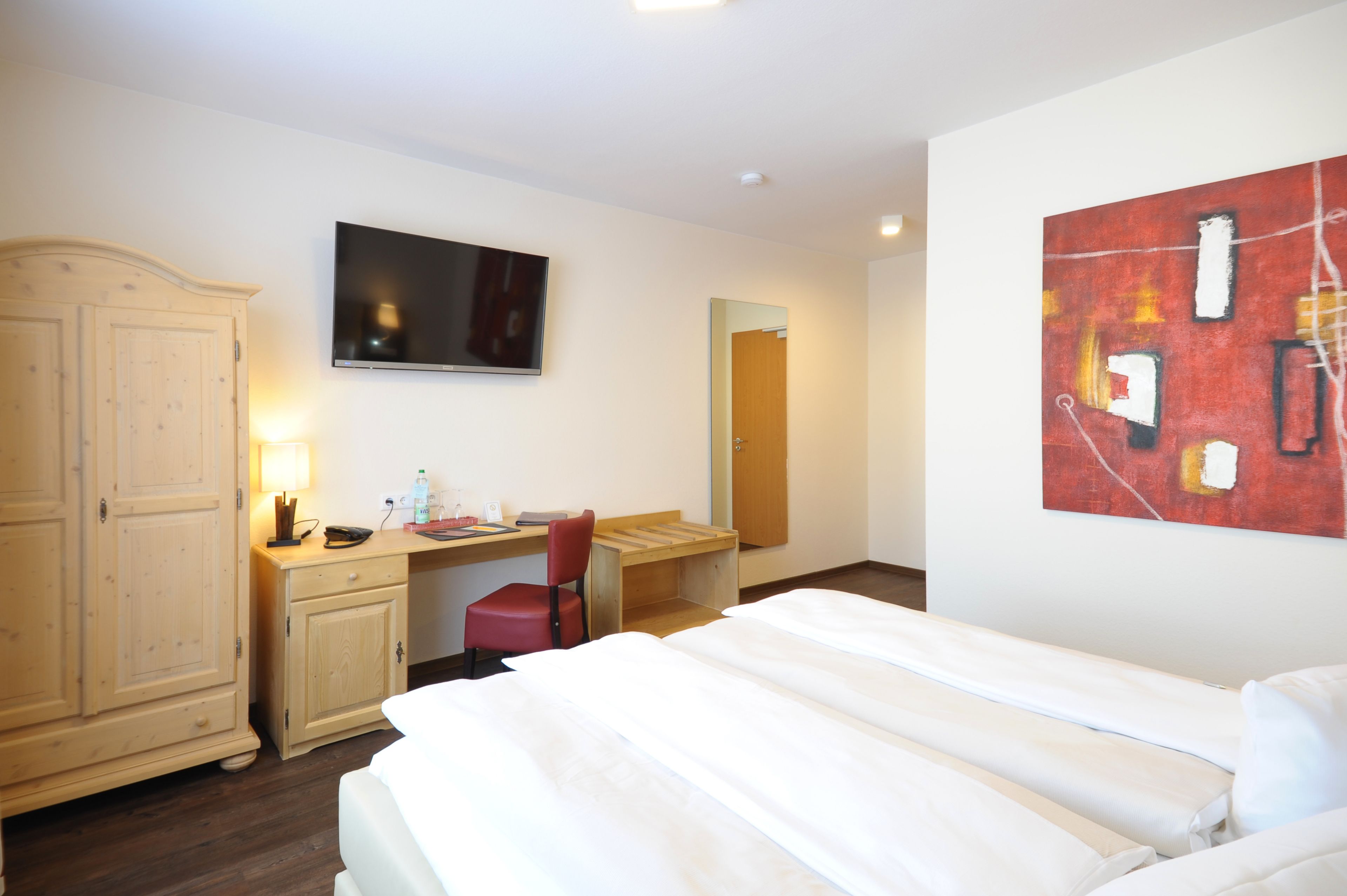 A hotel room with a bed, a desk, a chair, a television, and a wardrobe.