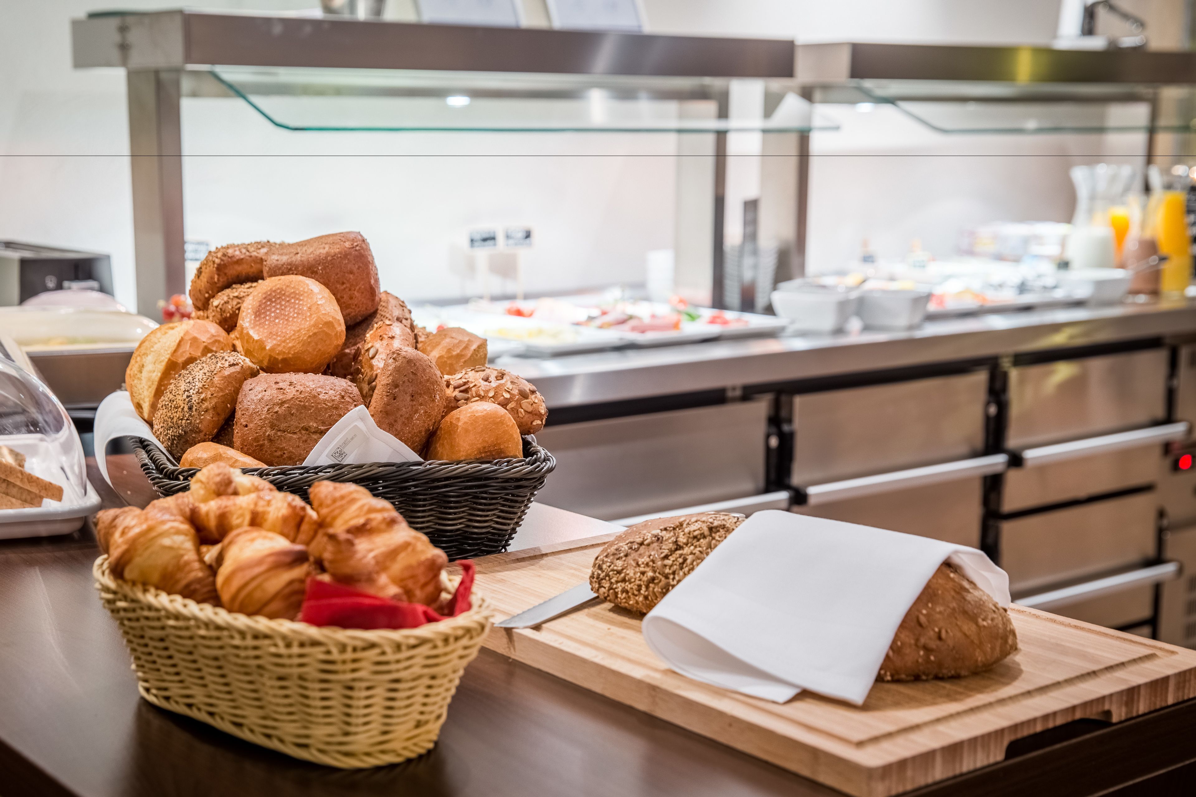 A buffet with various breads and pastries, including croissants and a loaf of bread on a cutting board.