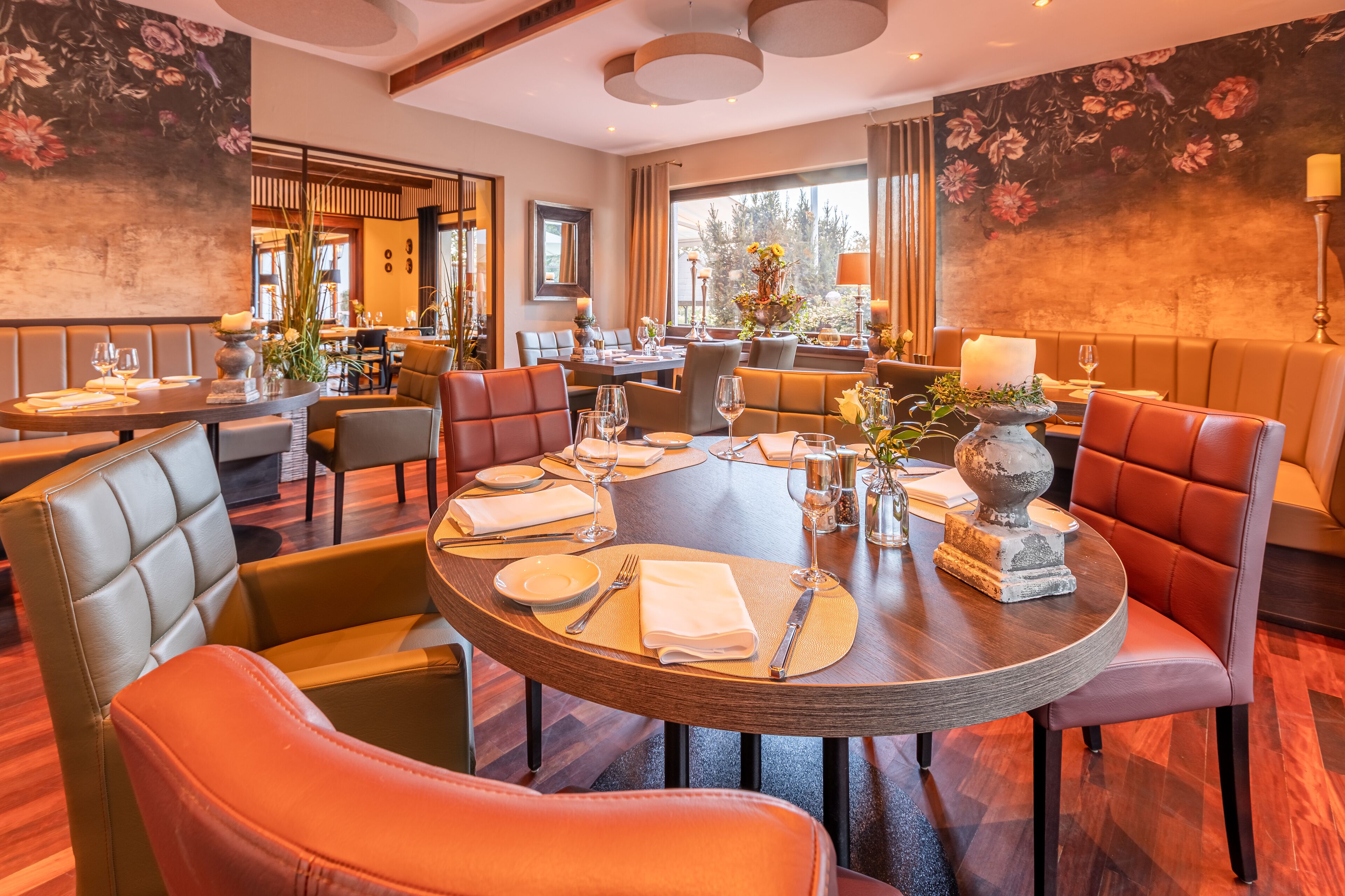 A restaurant with round tables, leather chairs, and floral wall art.