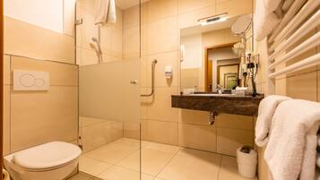 A modern bathroom with a glass-enclosed shower, a toilet, a sink with a mirror, and a towel rack.