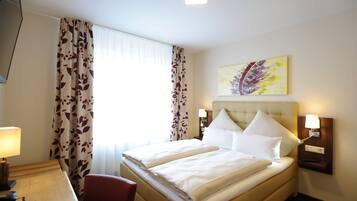 A hotel room with a double bed, a desk with a lamp, a chair, and a painting on the wall.