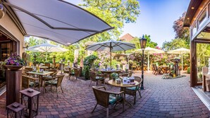 Une terrasse extérieure avec des tables et des chaises en osier, des parasols et une vue sur le jardin.