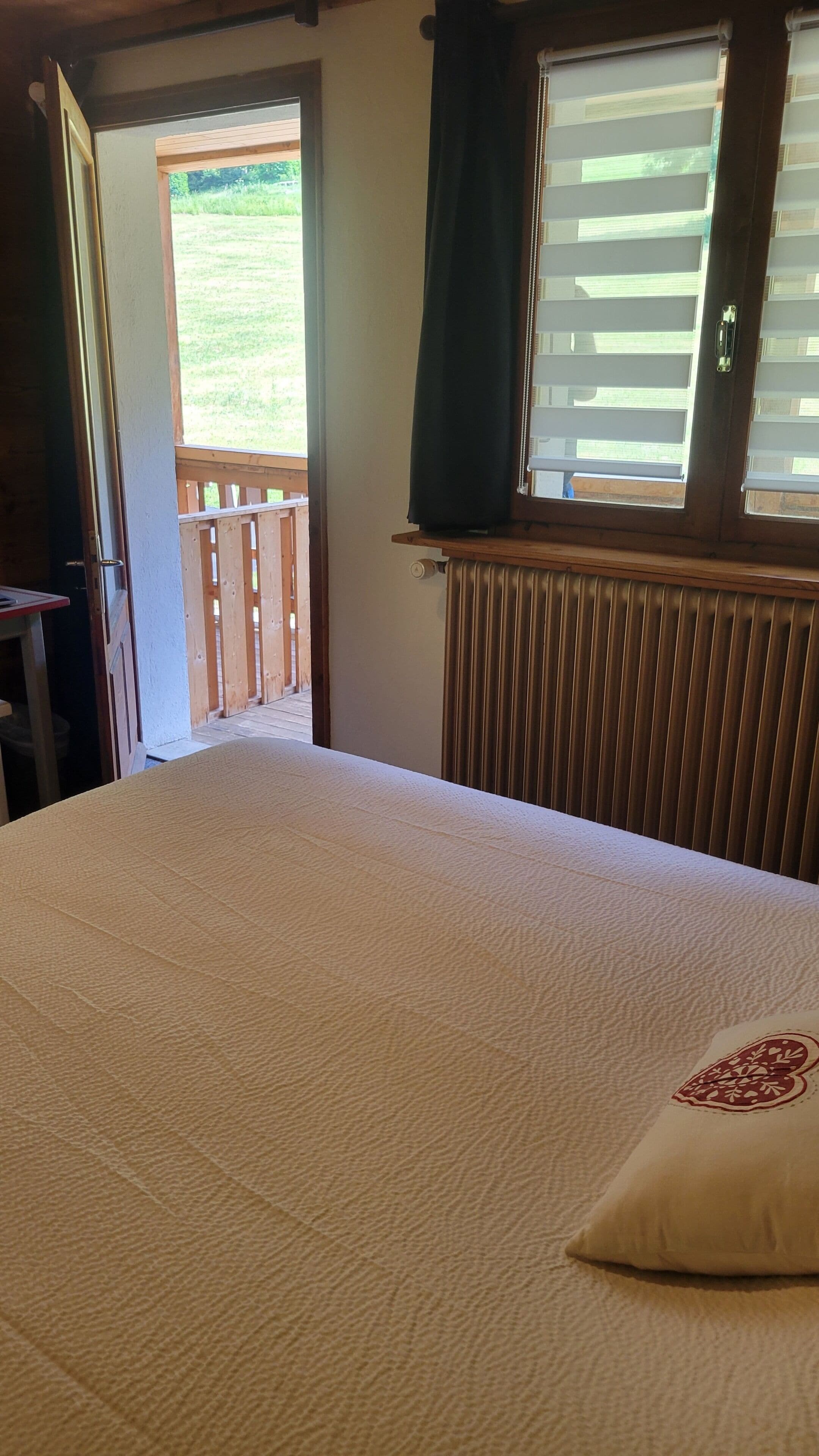 A bedroom with a bed, a window with curtains, a radiator, and a view of a garden.
