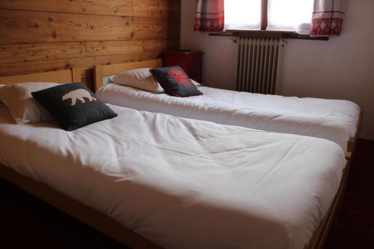 A room with two beds, wooden headboards, a window with curtains, and a radiator.