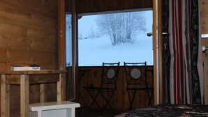 A wooden cabin room with a bed, a small table, and a view of a snowy landscape through a window. - Logis HOTEL Restaurant U'FREDY (La Clusaz)