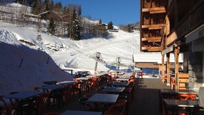 A ski resort restaurant with outdoor seating overlooking a snowy mountain slope. - Logis HOTEL Restaurant U'FREDY (La Clusaz)