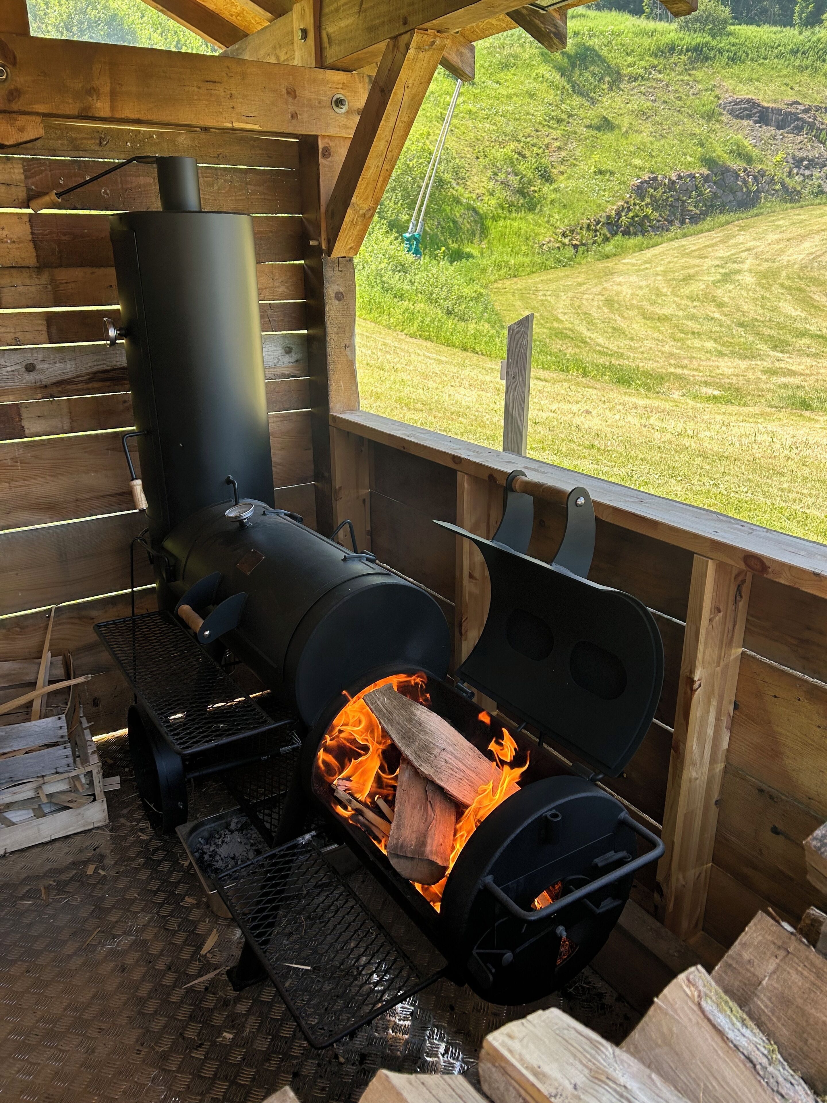 Ein Kaminofen mit Feuer im Inneren, eingebettet in eine Holzkonstruktion mit Blick auf eine grüne Landschaft.