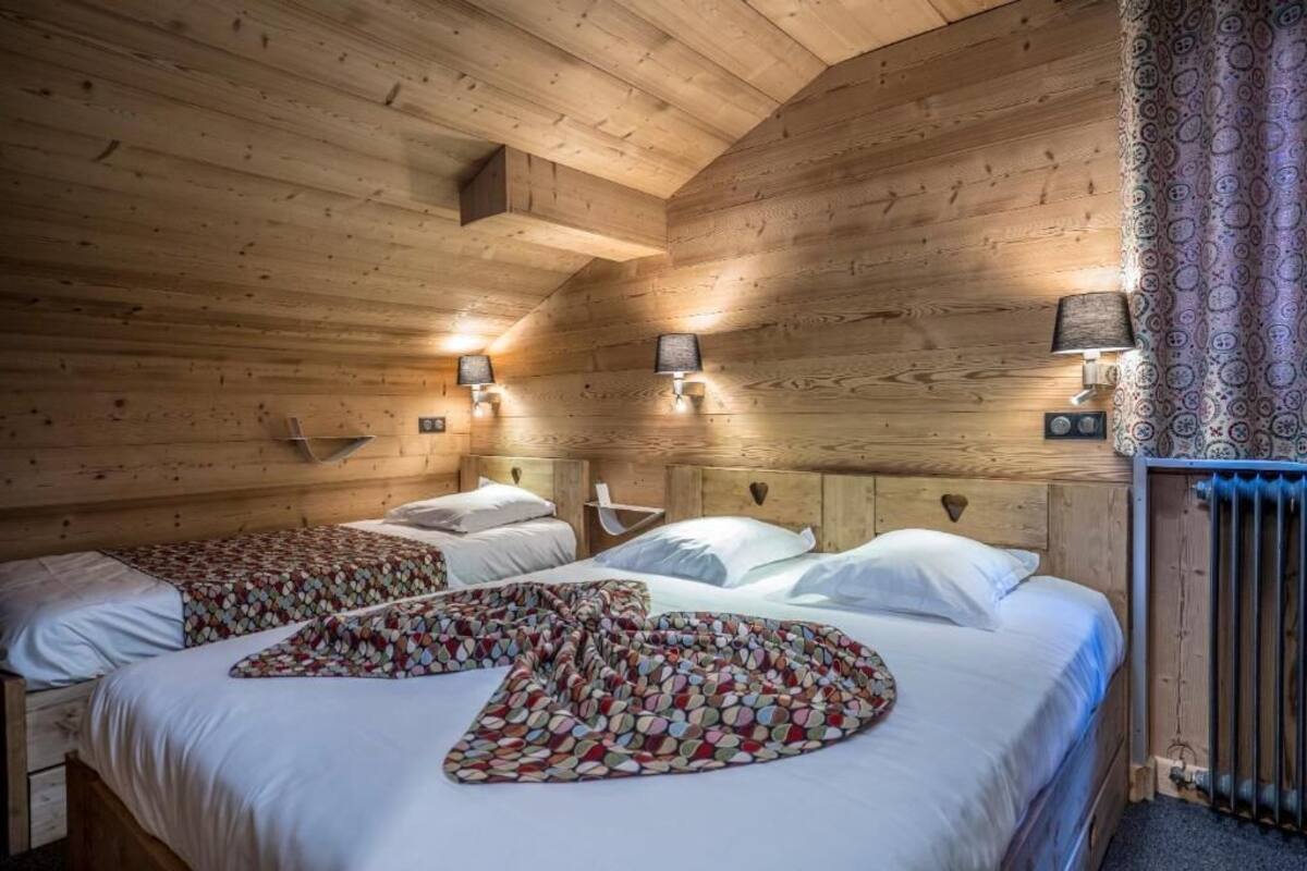 A wooden cabin-style room with two beds, each with a headboard, and a patterned throw blanket on the bed in the foreground.