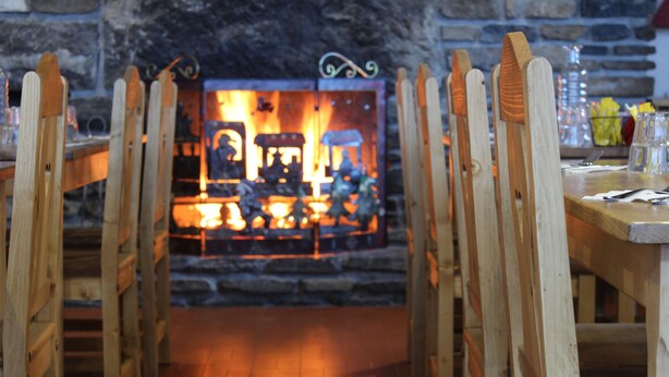 A restaurant with wooden chairs and tables arranged in front of a fireplace. - Logis HOTEL Restaurant U'FREDY (La Clusaz)