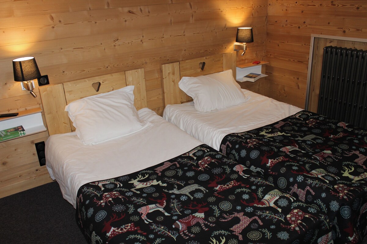 A double bed with white linens and a patterned bedspread, two bedside tables with lamps, and a wooden headboard.