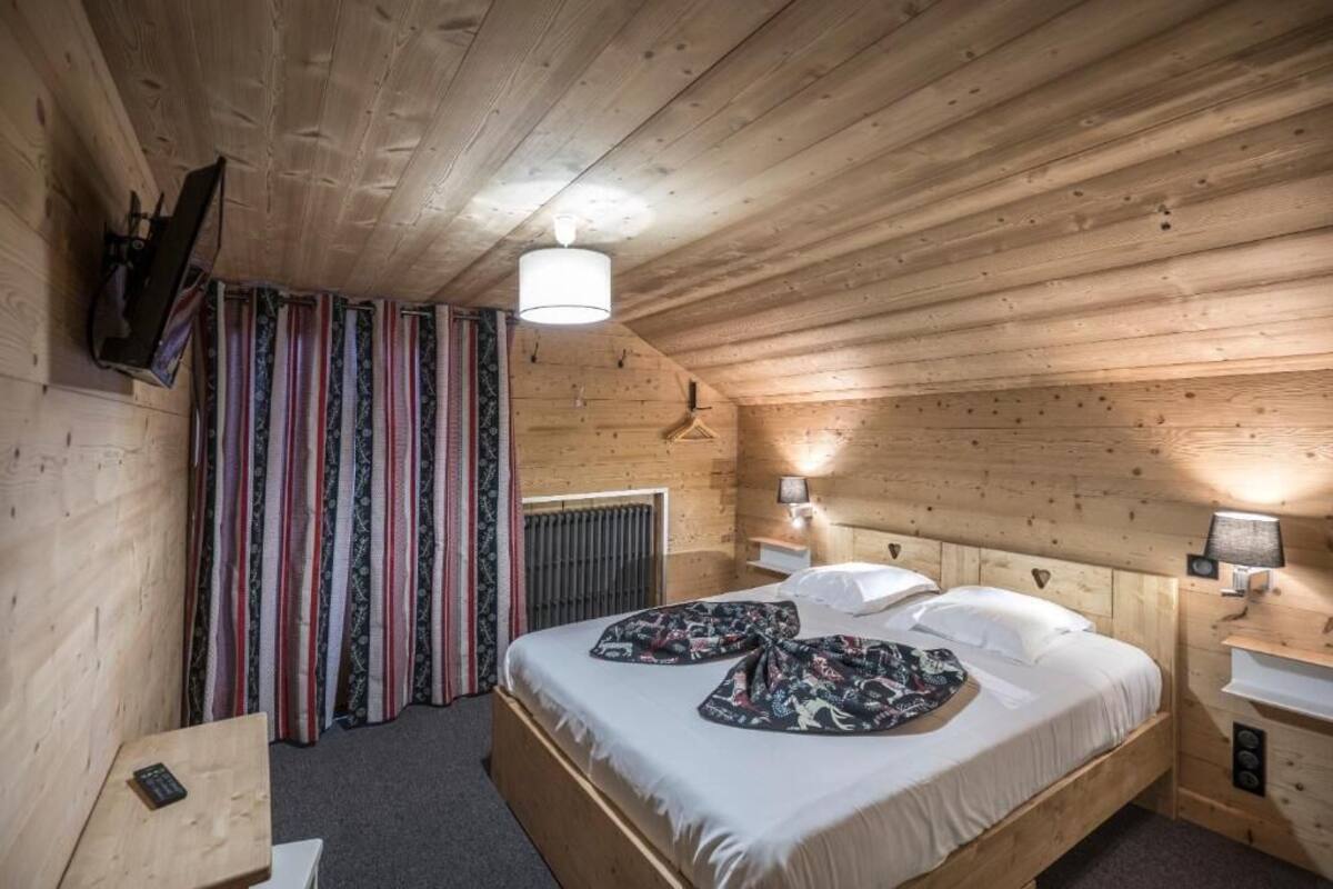 A wooden cabin room with a bed, bedside lamps, a hanging TV, and a radiator.
