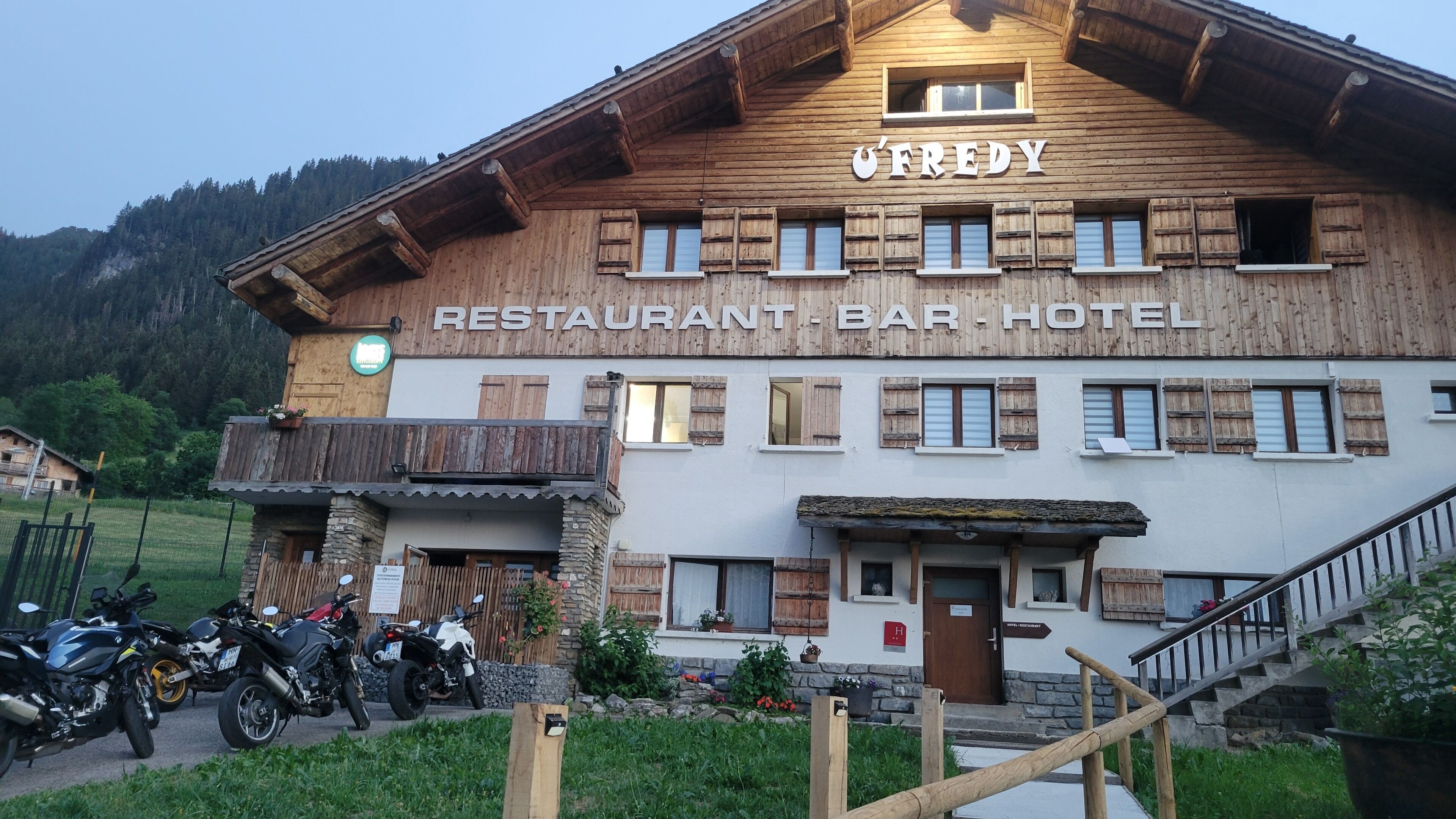 A wooden building with a sign that reads 'RESTAURANT BAR HOTEL.' There are motorcycles parked in front, and a staircase leading to the entrance.