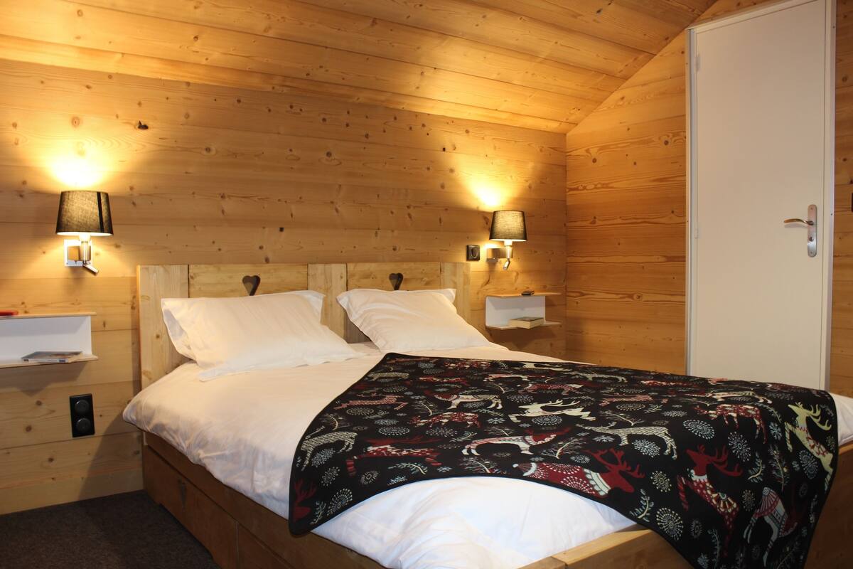 A wooden-paneled room with a bed, two wall-mounted lamps, and a white wardrobe.