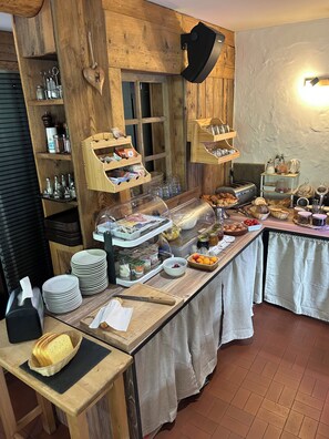A buffet setup with various food items, a wooden interior, and a counter with plates and utensils. - Logis HOTEL Restaurant U'FREDY (La Clusaz)