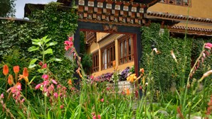 A traditional building with a wooden archway, surrounded by lush greenery and flowering plants. - Tiger Nest Resort (Paro)