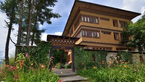 A traditional building with a multi-story structure, a stone wall, and a garden with various plants and flowers. - Tiger Nest Resort (Paro)