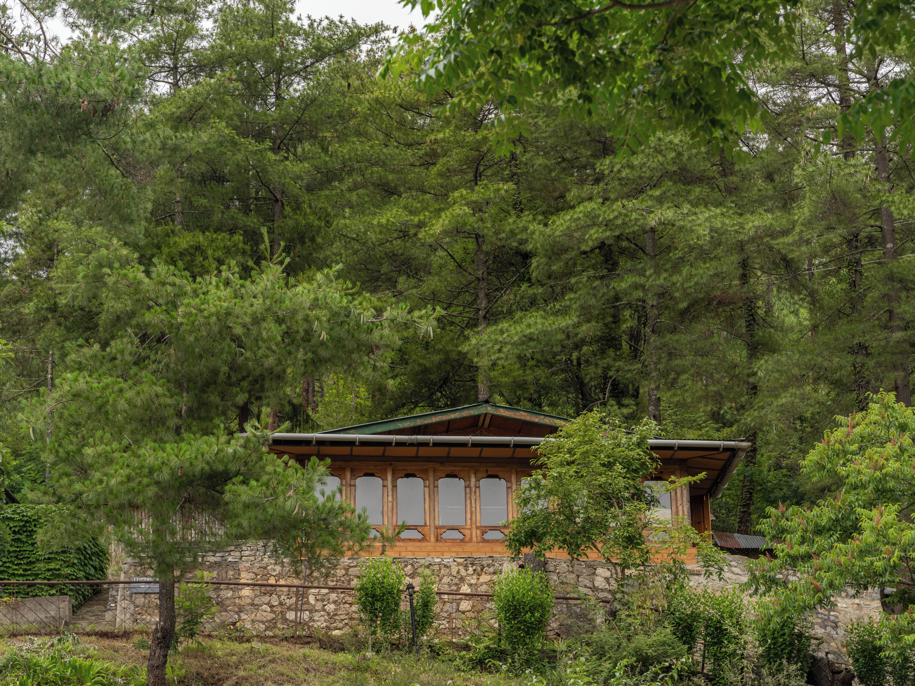 A stone building with a wooden roof, surrounded by dense green trees.