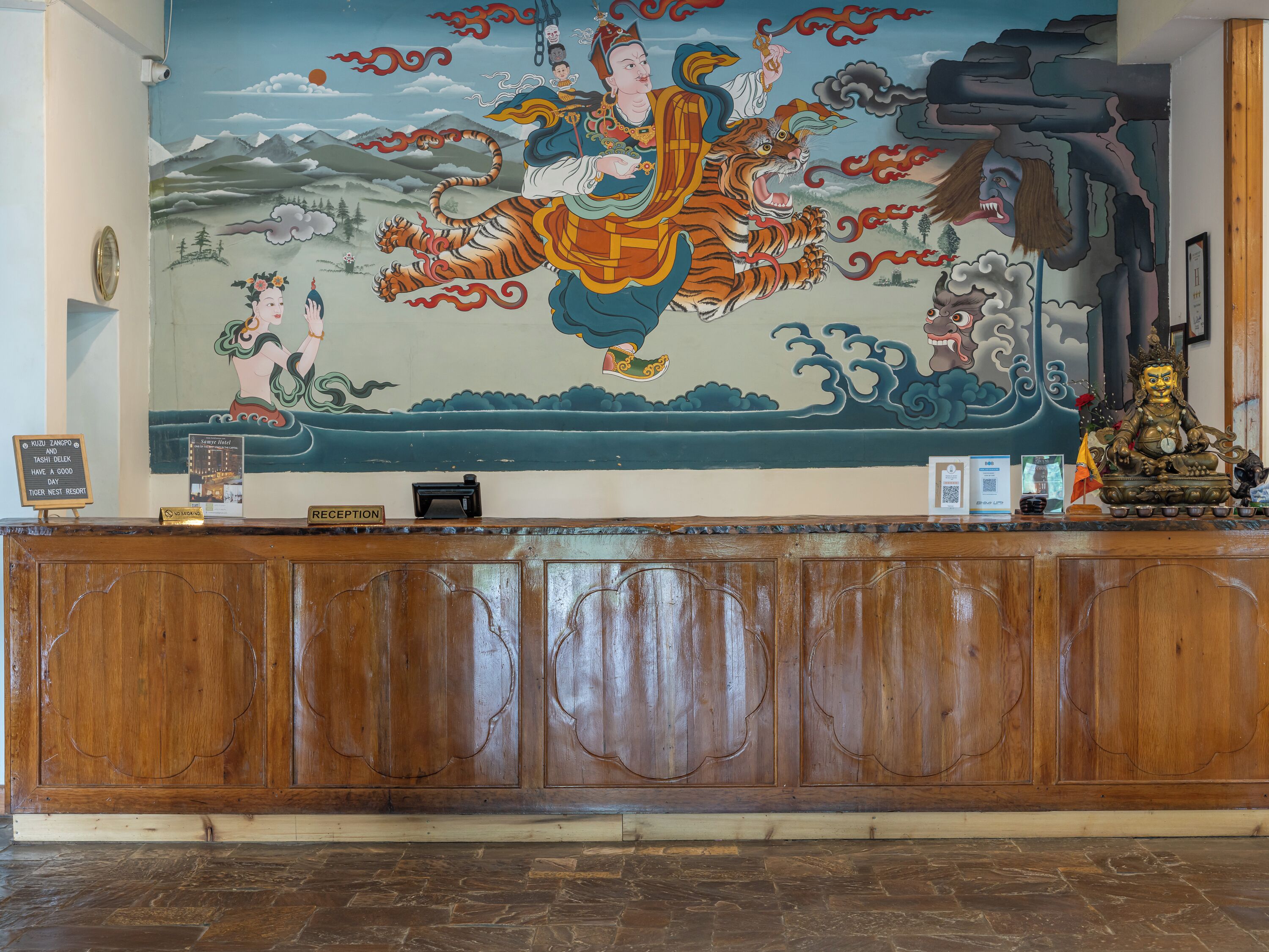 A reception desk with a mural depicting a figure riding a tiger, a Buddha statue, and a sign indicating a good day at Tiger West Resort.